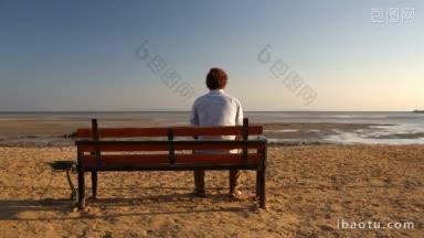 一个年轻人独自坐在沙滩上的长凳上